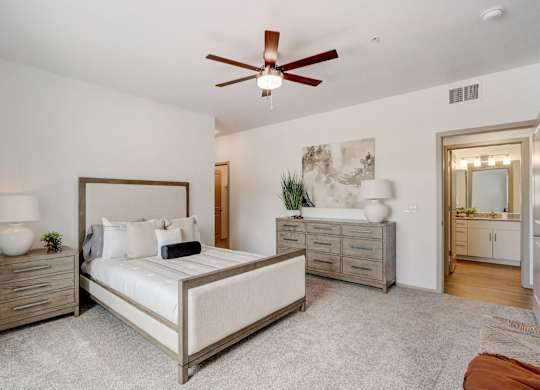A bedroom with a large bed, a ceiling fan, and a dresser.
