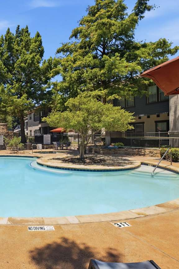 A small pool surrounded by trees and a building in the background.