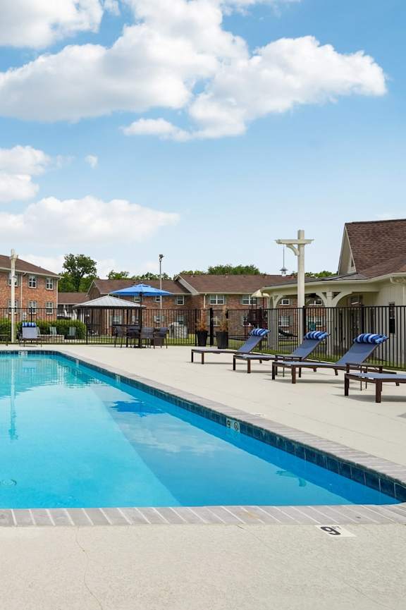 A large swimming pool surrounded by a fence and lounge chairs.