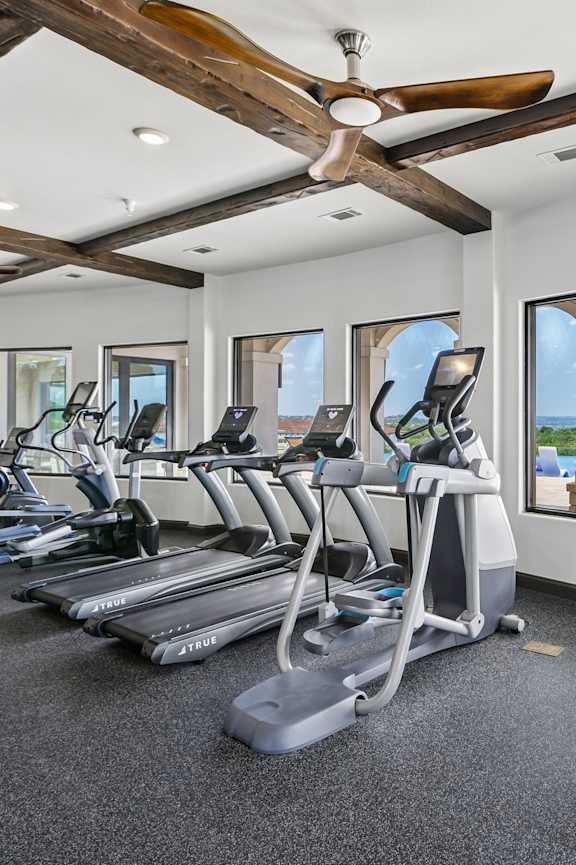 A gym with a row of treadmills and a fan.