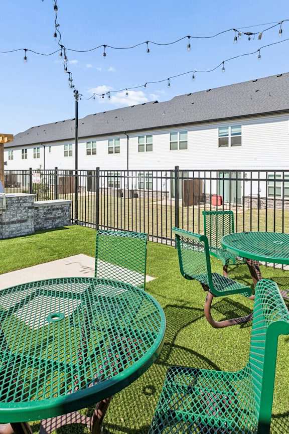 A patio with green chairs and tables is surrounded by a black fence.