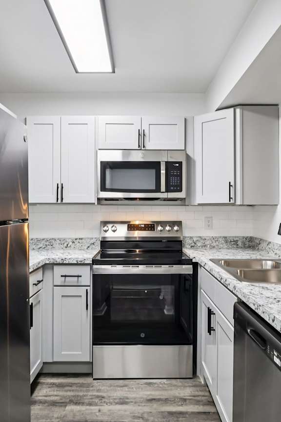 A kitchen with a refrigerator, microwave, oven, and sink.