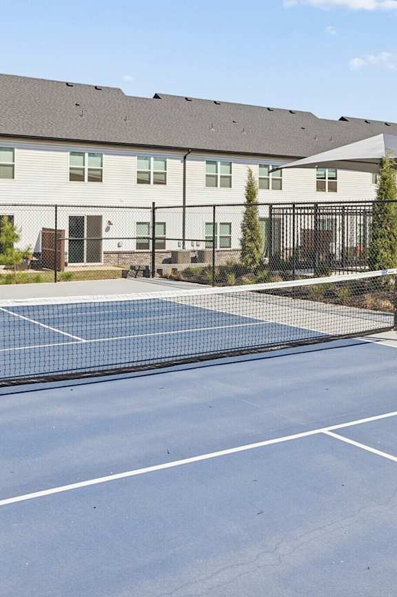 A tennis court is surrounded by a fence and a building.