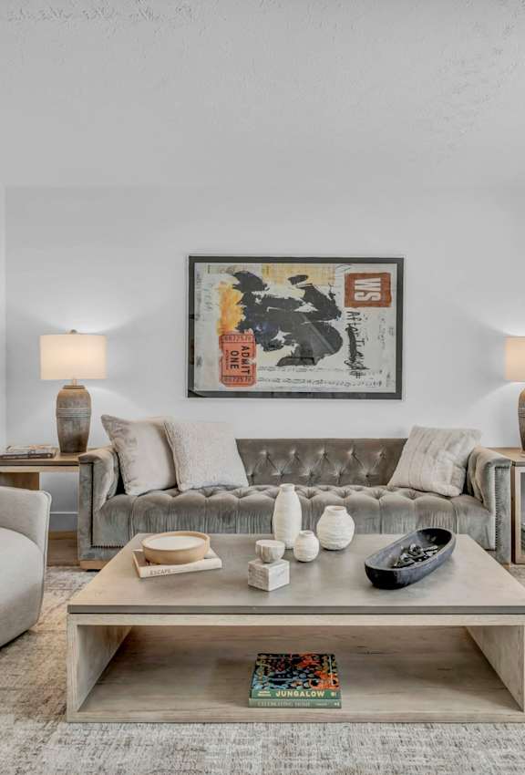 A living room with a grey couch, two chairs, a coffee table, and a painting on the wall.
