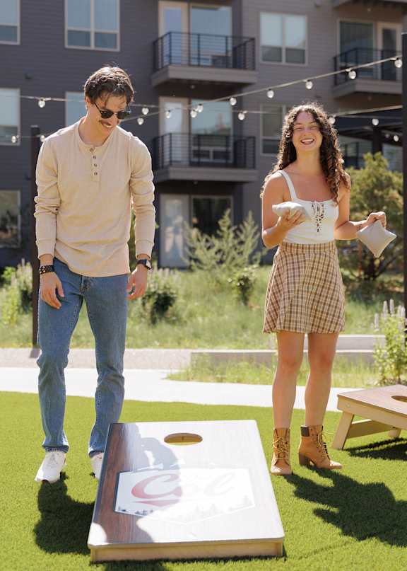A man and a woman are playing a game of cornhole in a grassy area.