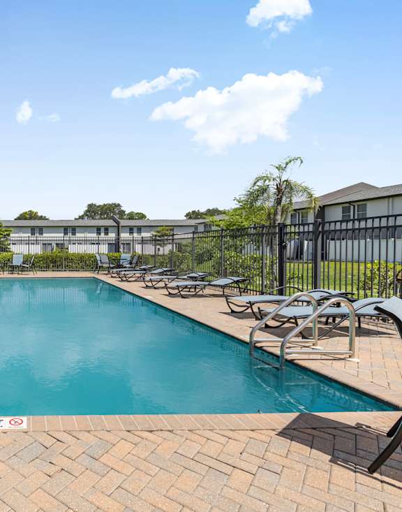 A swimming pool surrounded by lounge chairs and buildings in the background.