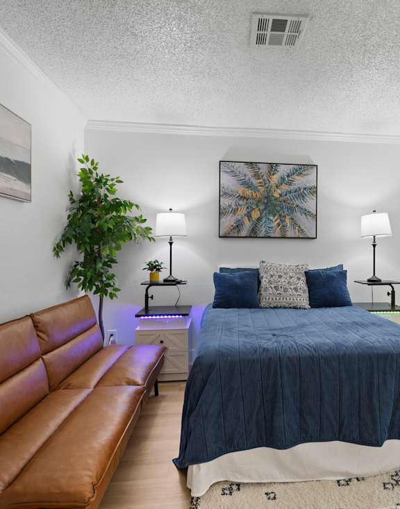 Furnished one bedroom apartments at Fusion Orlando with a bed with a blue comforter and a brown leather couch to the left.