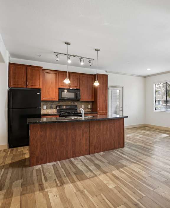 A kitchen with wooden floors and a black refrigerator.