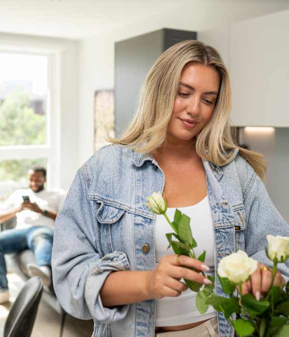 A woman in a denim jacket is holding a bouquet of white roses.