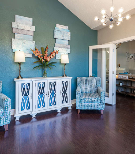 A room with a blue wall and a white end table with a vase of flowers on it.