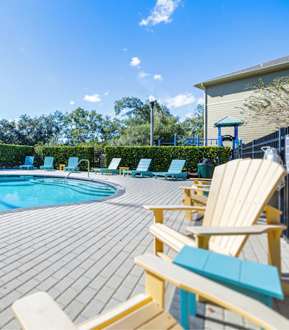 A pool surrounded by wooden deck chairs and hedges.