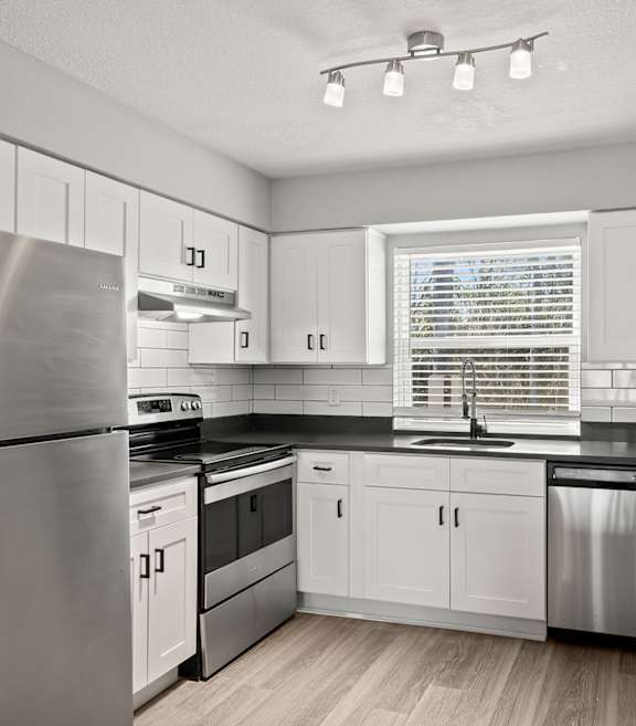 A kitchen with white cabinets and stainless steel appliances at Mandarin Bay Apartments.