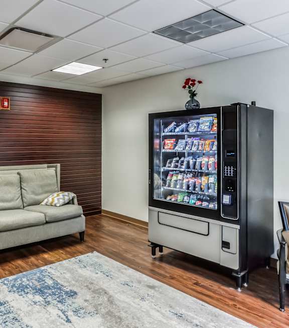 A room with a couch, chairs, and a vending machine.