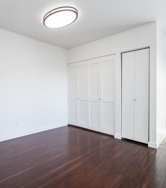 A room with white walls and a wooden floor with a white door and a white wardrobe.