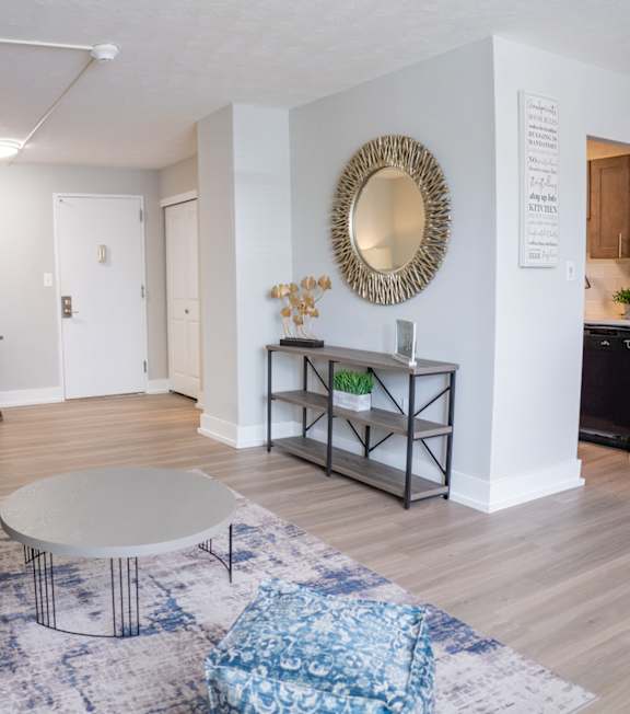 A living room with a grey couch, a white coffee table, and a round mirror on the wall.