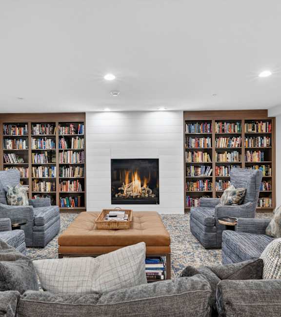 A living room with grey couches, a coffee table, and a fireplace with bookshelves above it.