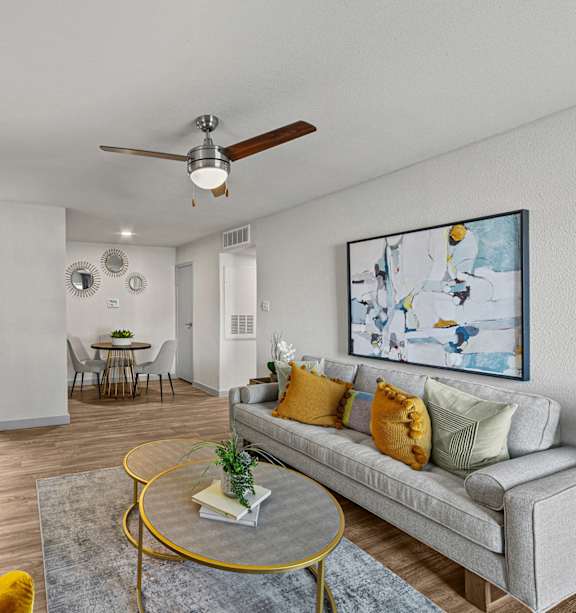 A living room with a grey couch, a yellow chair, a round table, and a painting on the wall.