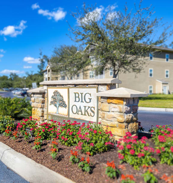 A sign for Big Oaks is surrounded by flowers and a tree.