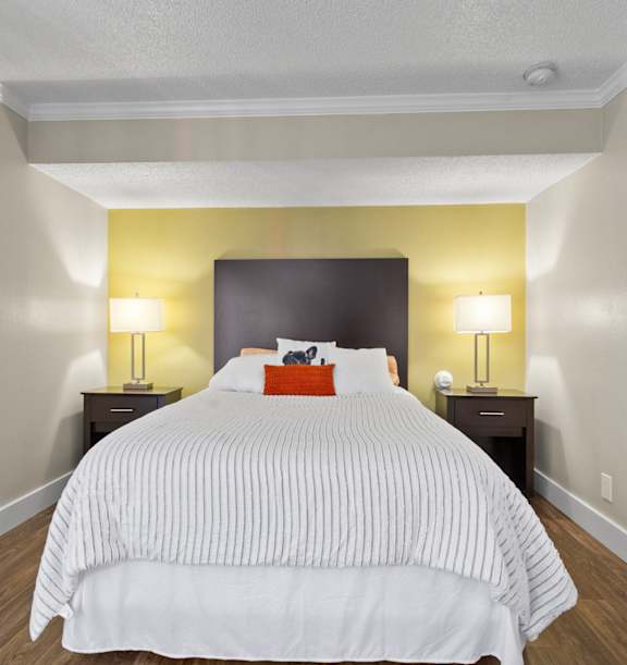 Furnished one bedroom apartments at Fusion Orlando with a bed with a white comforter and a yellow wall.