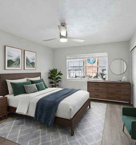 Watermarc Apartments bedroom with an overhead fan, large window, and a bed with a wooden bed frame, white comforter, and blue and green accents.