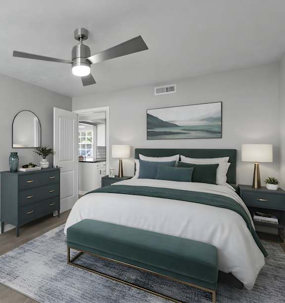 A bedroom at Watermarc Apartments in Lakeland, FL with a ceiling fan, closet with white sliding door, and a bed with a white comforter and green accents.
