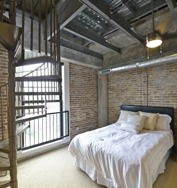a bedroom in a loft with a bed and a spiral staircase