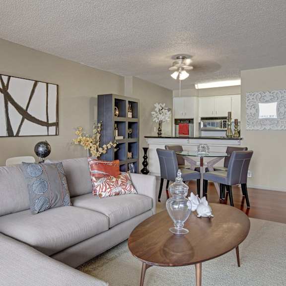 A living room with a view of a kitchen, table and chairs, a couch, a coffee table, and lamps at Capitol Towers. 