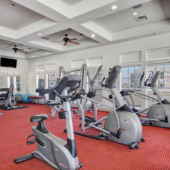 A gym with cardio equipment and windows on the wall at Liberty Pointe Apartments. 