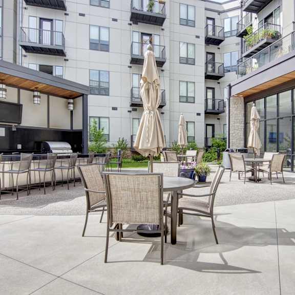 An outdoor patio area with tables and chairs, a TV, countertops with multiple grills, and green spaces at Residence at the COR Apartment Homes. 