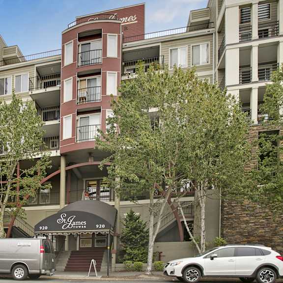 The street view of the brick, white, and gray apartments at St. James Tower Apartments with trees in the sidewalk. 