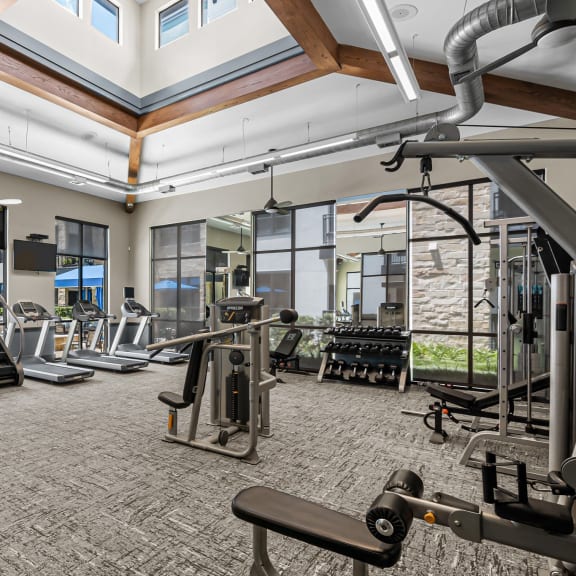 a gym with cardio equipment and weights in a building with windows
