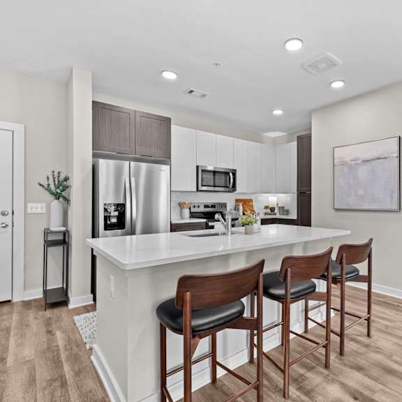 A kitchen with a white counter top and wooden bar stools.