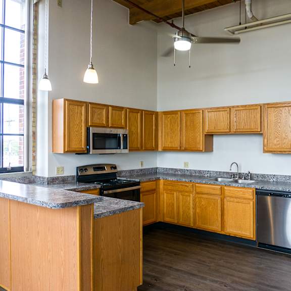 Loft kitchen with wood cabinets and pendant lights at Off Broadway Apartments