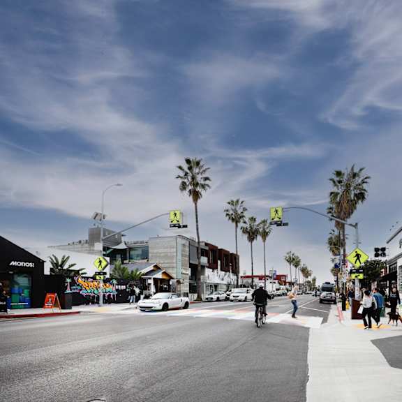 A street scene with a white car driving on the road and people walking on the sidewalk.
