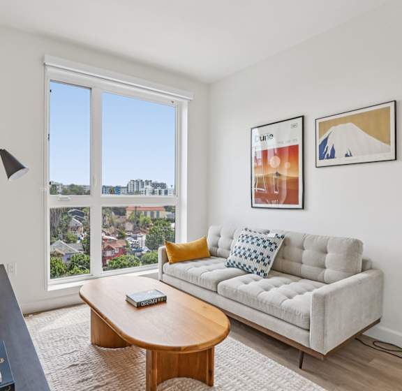 A living room with a couch, a coffee table, and a large window overlooking a cityscape.