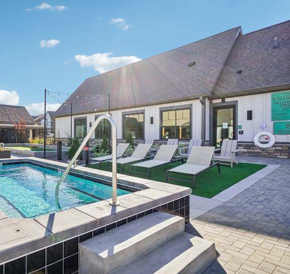 a swimming pool in front of a house with a pool and lounge chairs