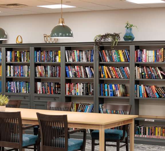 A room with a long table and a bookshelf filled with books.