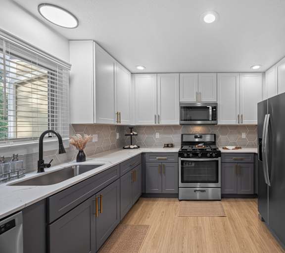 Apartments Near UNC Asheville - Verde Vista - Kitchen with Wood-Style Plank Flooring, Quartz Countertops, Two-Tone Cabinetry, Deep Sink, Range, Microwave, and Refrigerator.