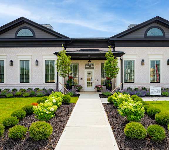A two-story house with a front yard landscaped with bushes and flowers.