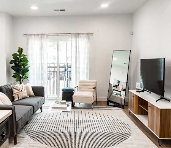 A living room with a black couch, a white chair, a television, and a mirror.