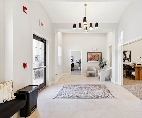 A large bedroom with a queen-size bed, a dresser, decorations, a view of the en suite bathroom, window, and nightstands at Quail Landing Apartment Homes. 