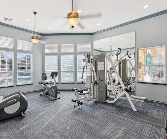 A gym with cardio machines, windows, TVs, and weights at Quail Landing Apartment Homes. 