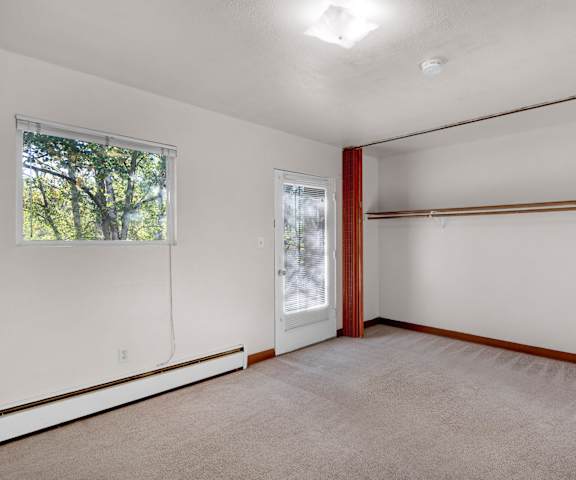 An empty living room with carpeting and a door to a balcony at Country Lane Apartments. 