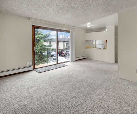 An empty living room with carpeting and a door to the balcony at Deer Park Apartments. 
