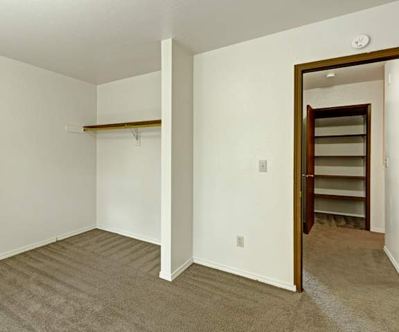A large, empty carpeted bedroom with overhead lighting and a closet at the Glen Apartment Homes. 