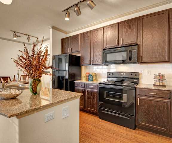 A spacious kitchen with black appliances, marble countertops, and wooden cabinets with decorations at Liberty Pointe Apartment Homes. 