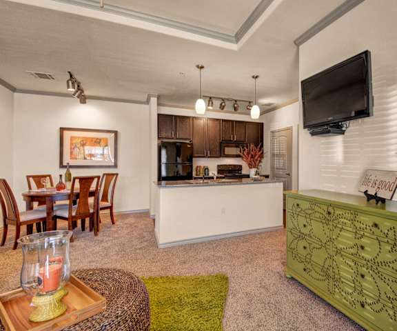 The living room with a couch, plush chairs, coffee table, decorations, a TV, and view of the dining room and the kitchen at Liberty Pointe Apartment Homes. 