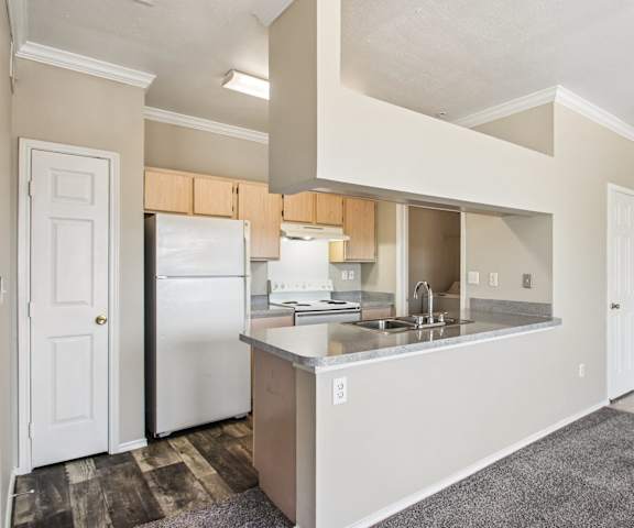 A large, modern kitchen with stainless steel appliances, bar counter with barstools, kitchen utensils, light countertops with lots of room, and large wooden cabinets at Sycamore Farms Apartment Homes. 