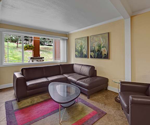 The resident lounge with a leather couch and a plush chair with coffee tables, a rug, calla lily wall art, and a window at Taiga Apartment Homes. 