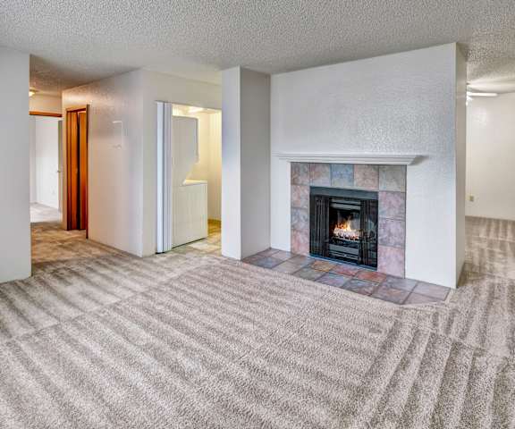 A large, empty living room with carpeting and a fireplace at Terrace on the Lake Apartment Homes. 